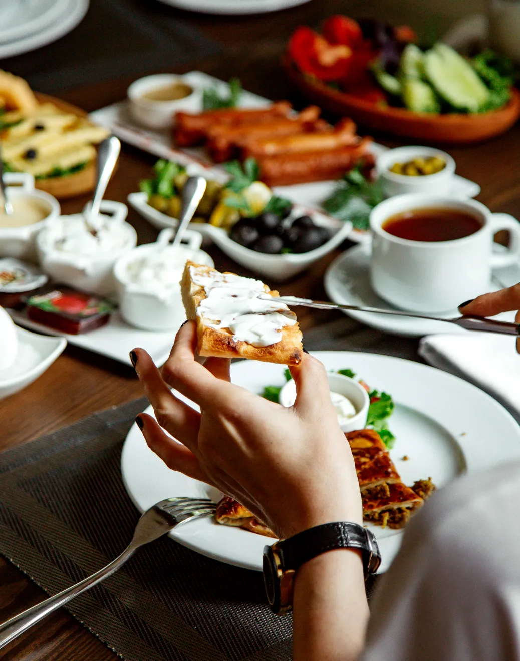 A person spreading a piece of bread with sauce.